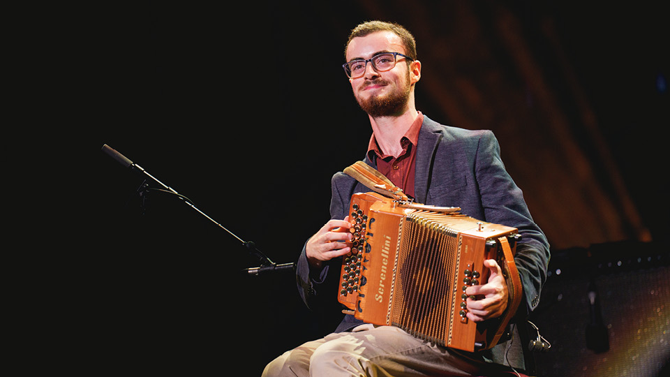 Young adult musician playing music in floodlight on stage  